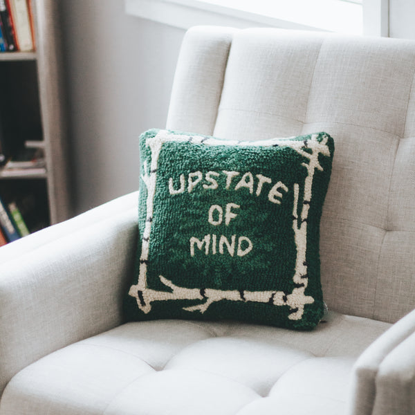 Upstate of Mind Handmade Hooked Wool Decor Pillow made by Chandler4Corners. Pillow is sitting on the corner of a beige white cozy chair in a minimalist living room.