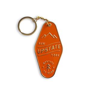 Upstate Motel Key Keychain in Burnt Orange. Chain, keyring, and raised text/illustrations are golden. Text reads: "UPSTATE, NEW YORK / Upstate of Mind".