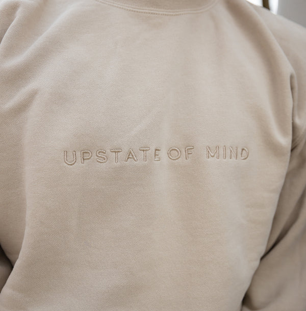 The Upstate of Mind Standard Stitch Crewneck in Ivory. Features an embroidered stitch text, "Upstate Of Mind", on the front of the crewneck.