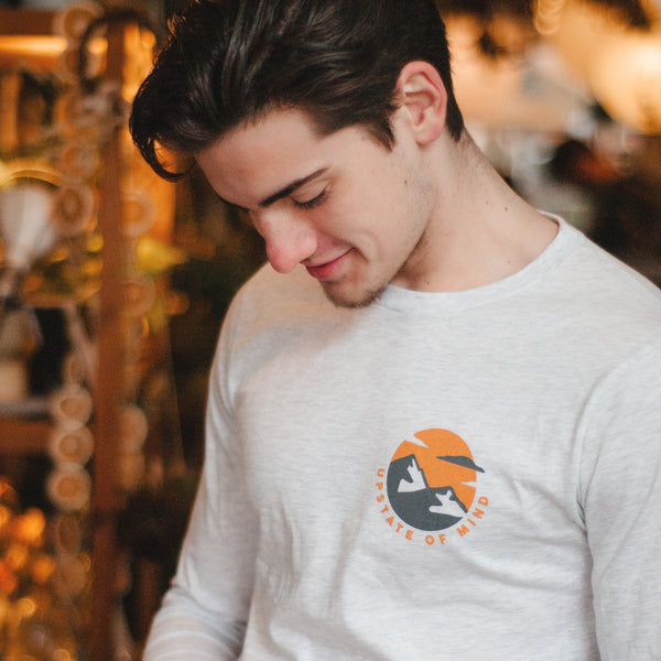 A model wearing the Upstate of Mind In The Clouds Longsleeve Tee in a moody, warmly light shop.