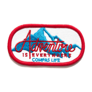 Photo of Adventure is Everywhere Patch. Red edges with blue mountains. "Adventure is everywhere" text is red. Compas Life logo is blue.